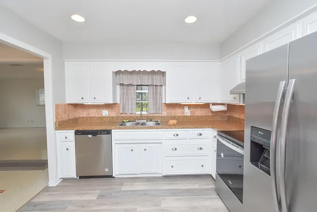 a kitchen with granite countertop a refrigerator oven a sink dishwasher and white cabinets with wooden floor