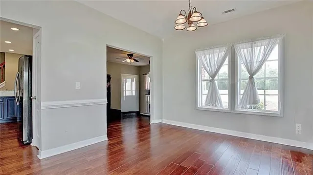 an empty room with wooden floor chandelier and windows