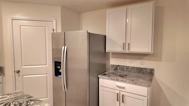 a kitchen with stainless steel appliances granite countertop a refrigerator a sink and white cabinets