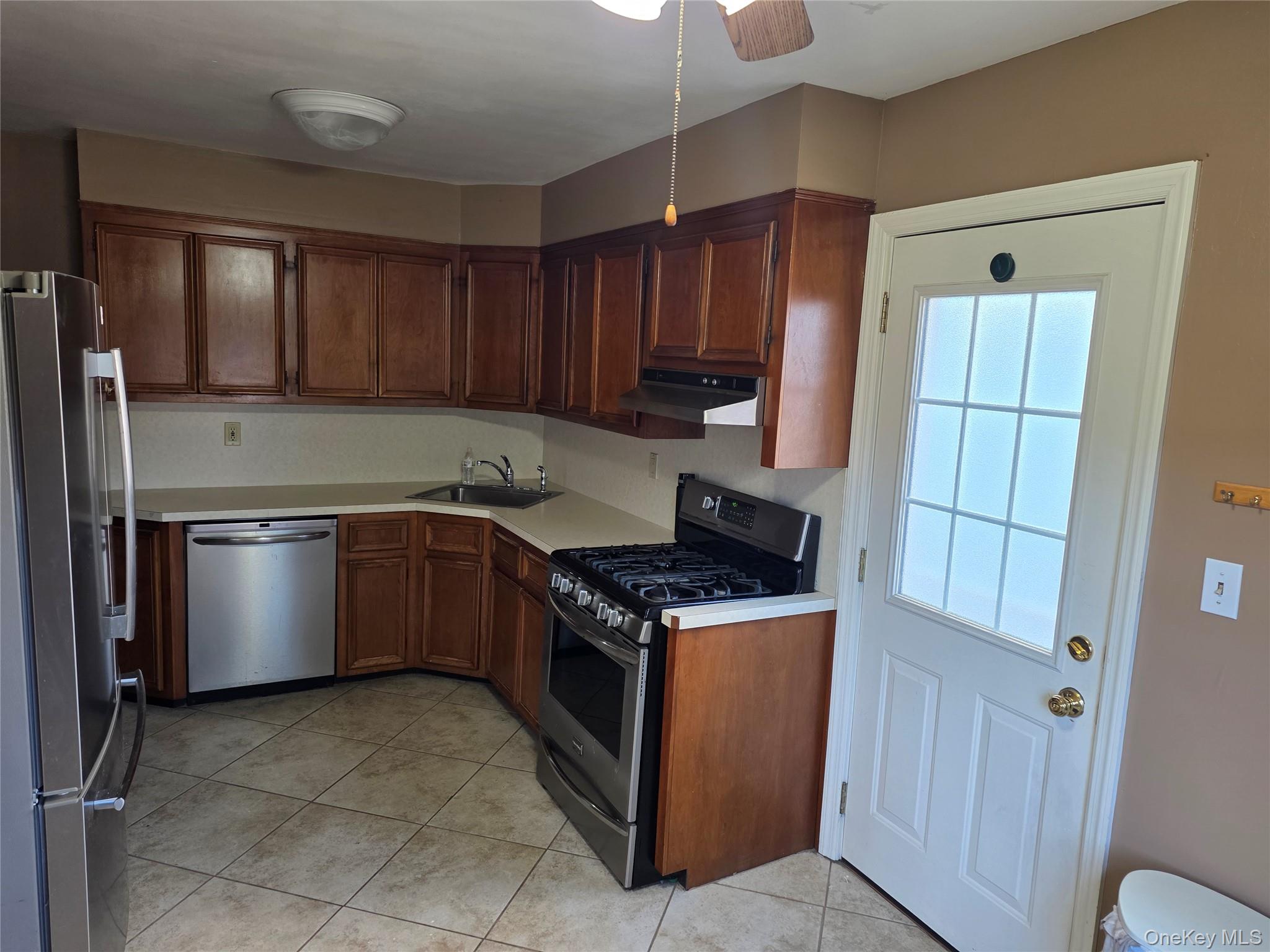 220 Raff Avenue Mineola, NY 11501 - Photo 3 of 22 Kitchen featuring stainless steel appliances, light countertops, light tile patterned flooring, under cabinet range hood, and brown cabinets