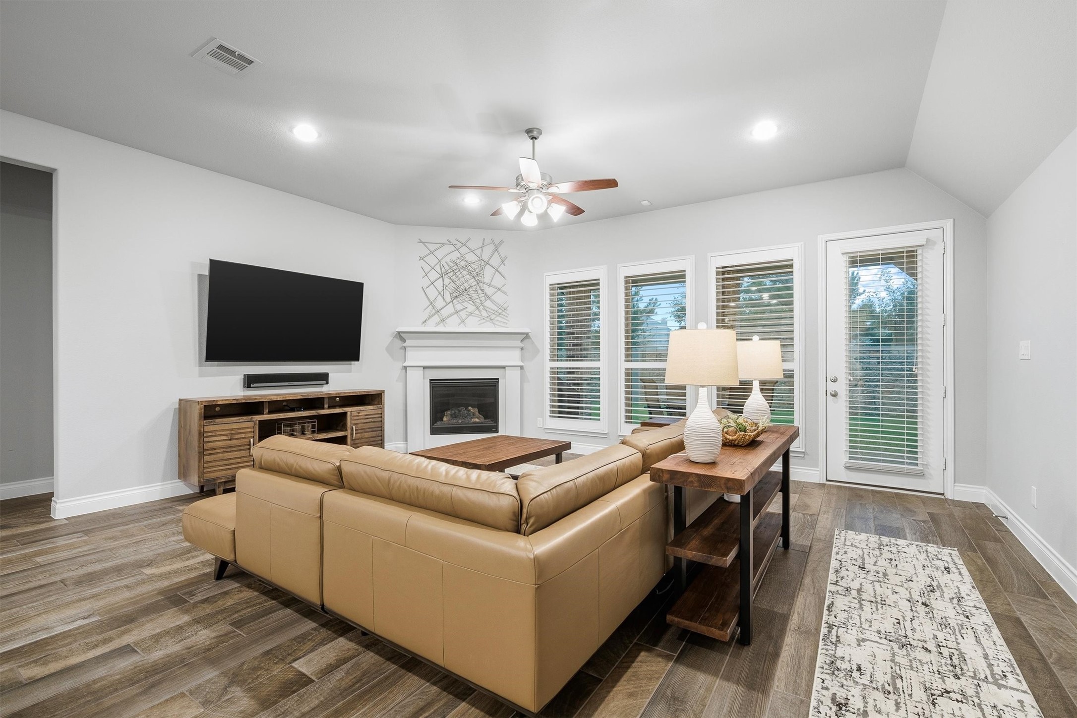 29118 Lantana Ridge Court Fulshear, TX 77441 - Photo 8 of 29 Gather in the inviting living room, showcasing a beautiful fireplace, multiple windows, and a modern ceiling fan that adds a touch of sophistication, the perfect blend of comfort and timeless style.