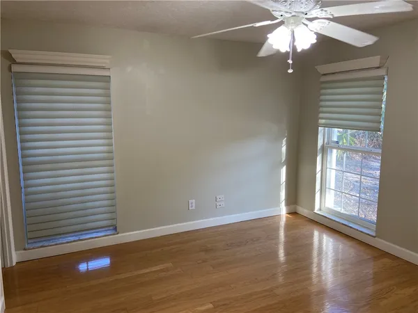 an empty room with wooden floor fan and windows
