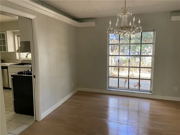a view of an empty room with wooden floor and a kitchen