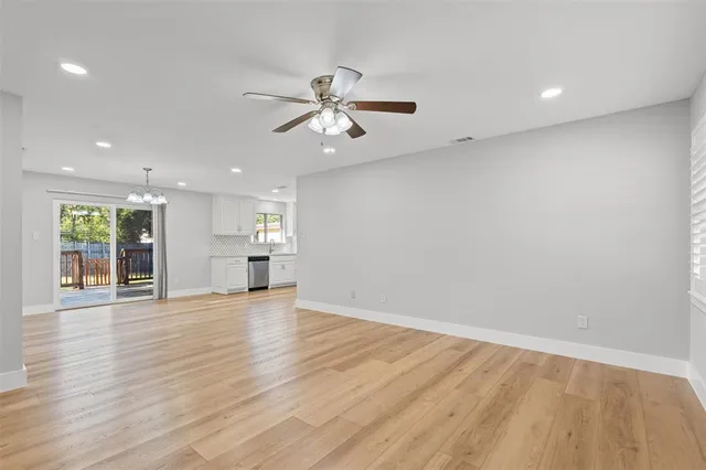 an empty room with wooden floor a ceiling fan and kitchen view