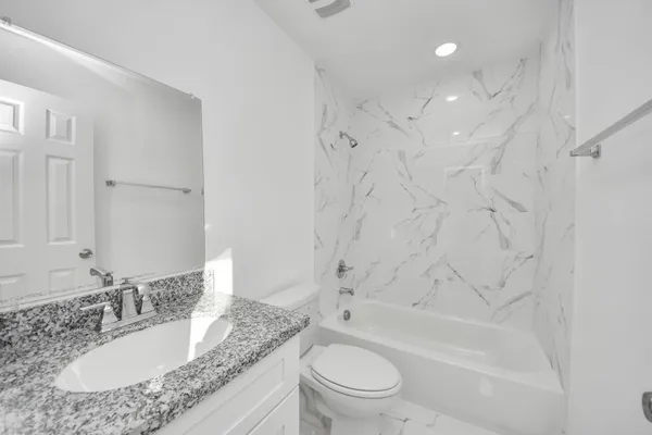 a bathroom with a granite countertop sink toilet mirror and bathtub