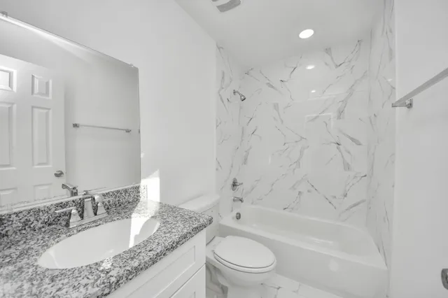 a bathroom with a granite countertop sink toilet mirror and bathtub