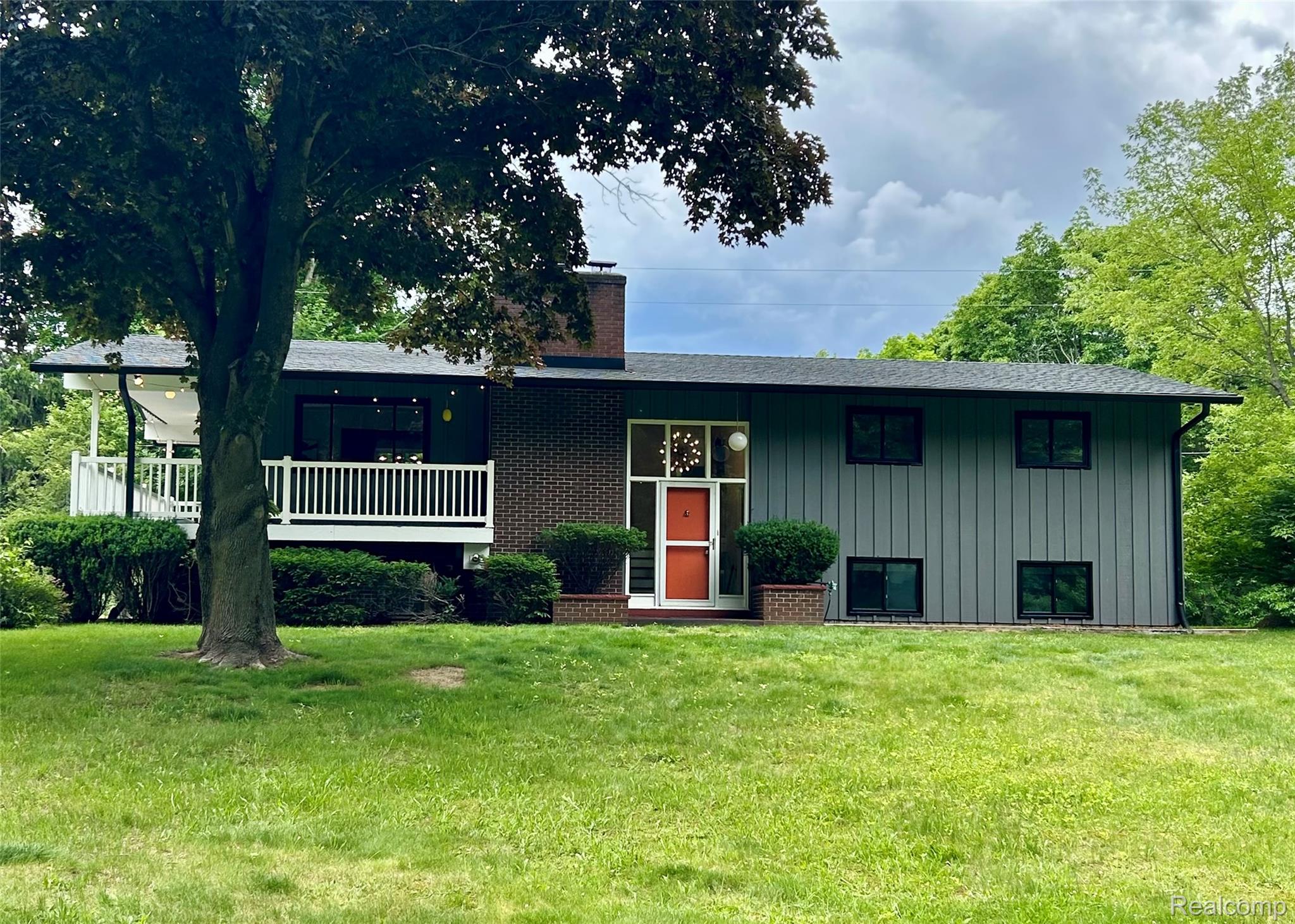 7333 Toma Road Dexter, MI 48130 - Photo 1 of 46 Mid-century modern exterior featuring vertical siding, a brick facade, a covered porch with white railings, and a prominent orange front door