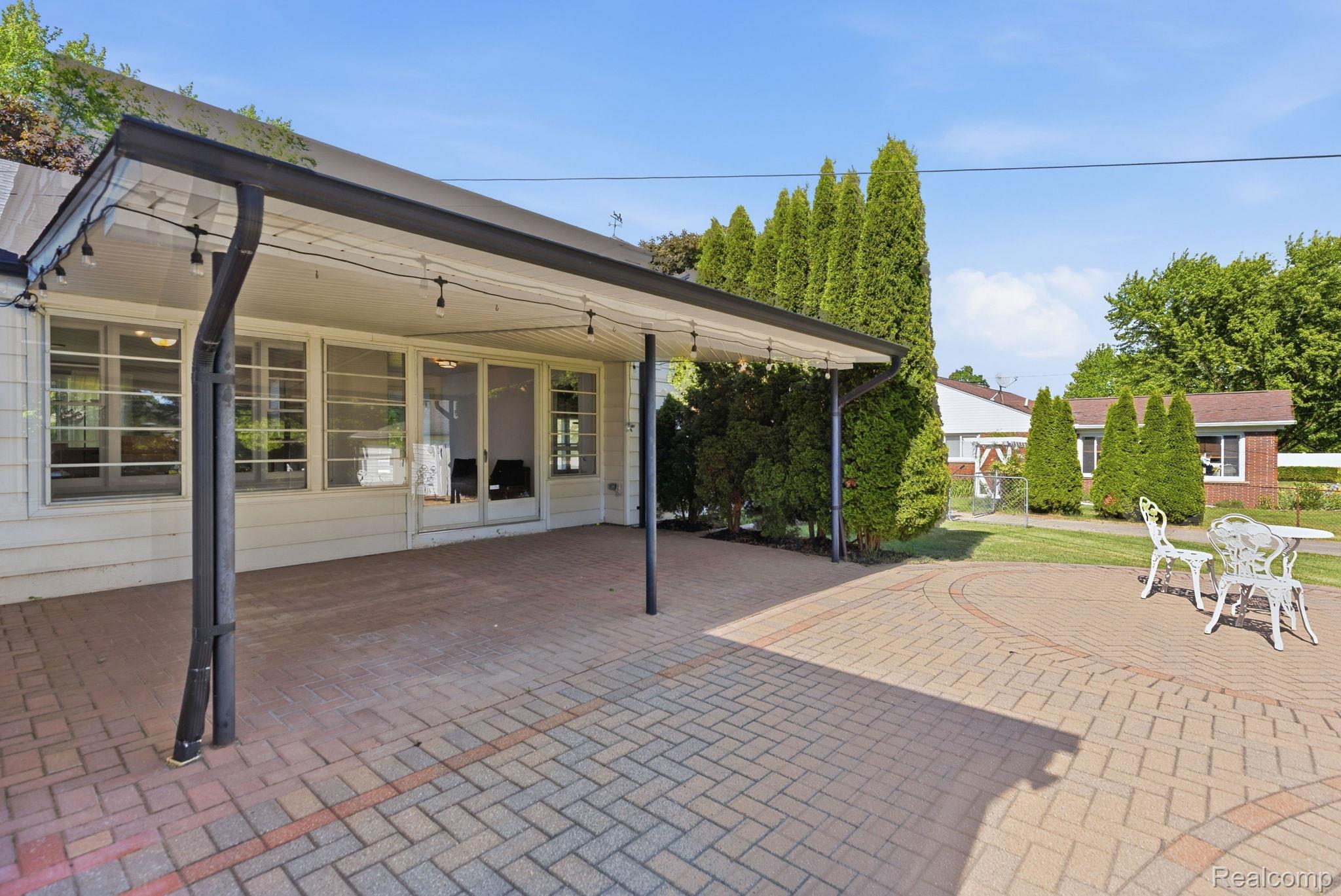 8710 32 Mile Road Washington, MI 48095 - Photo 47 of 60 Expansive brick paver patio featuring a covered awning with string lighting, multiple windows, and exterior access