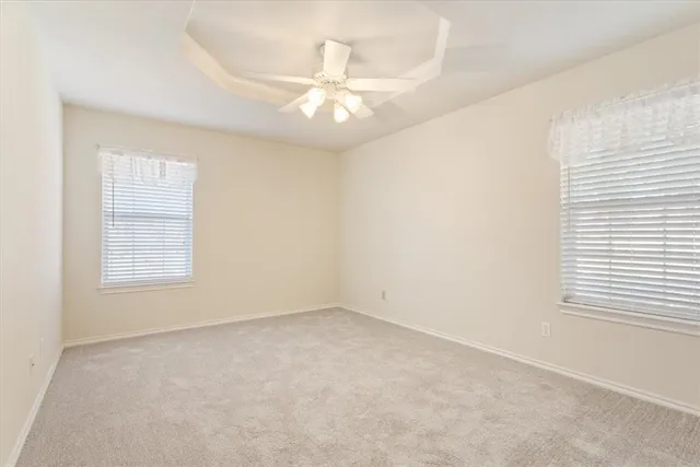 an empty room with a chandelier fan and windows