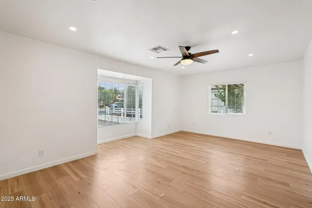 an empty room with wooden floor fan and windows