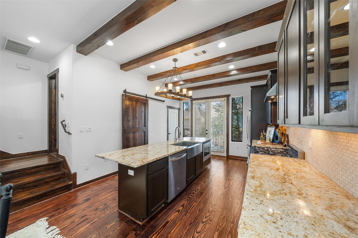 2601 Bevis Street, Unit E Houston, TX 77008 - Photo 17 of 47 Chef’s kitchen featuring granite countertops, a
large center island with farmhouse sink, and
rich cabinetry, all accented by striking exposed
wood ceiling beams. A rustic sliding barn door
reveals a spacious pantry, combining style with
practical storage.