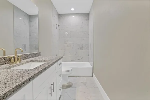 a bathroom with a granite countertop sink a toilet and bathtub