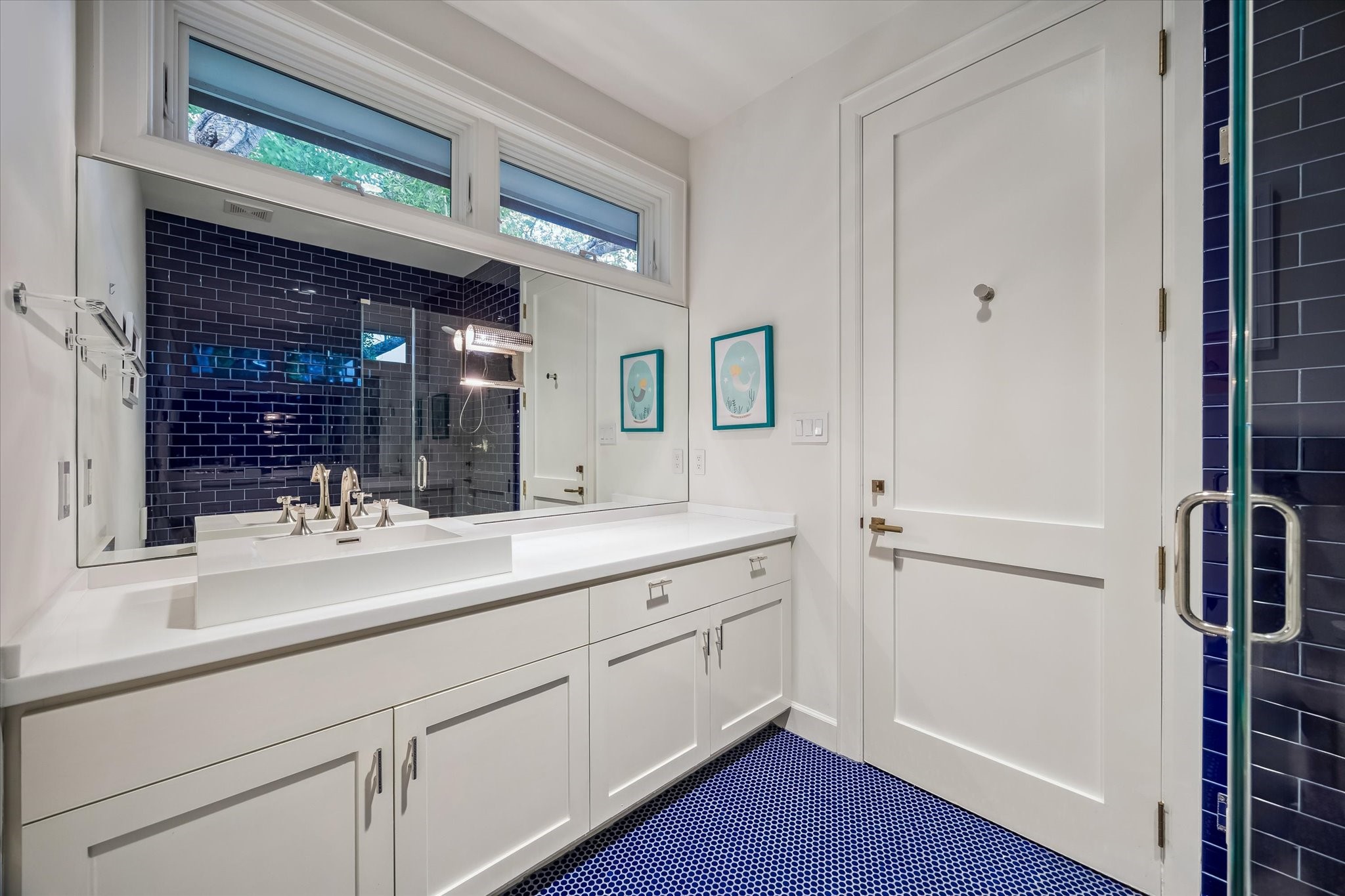 3706 Tangley Street Houston, TX 77005 - Photo 37 of 50 Guest Bathroom No. 2 pairs blue penny tile flooring with crisp subway tile walls, creating a fresh yet timeless contrast. Polished nickel hardware and a vessel sink add a refined, tailored finish to the space. Thoughtful natural light from western-facing and transom windows enhances the room’s bright, welcoming feel—an intentional design move, as guest baths are often meant to leave a lasting impression.