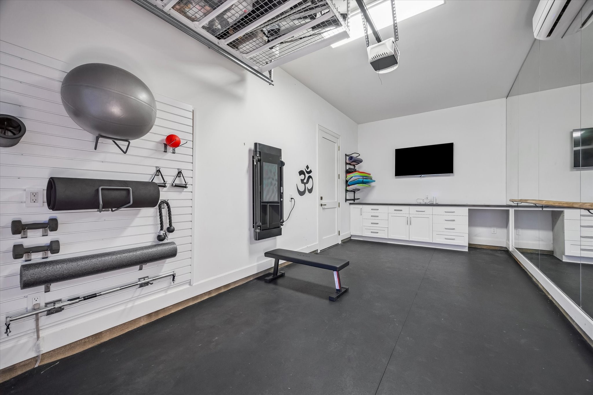 3706 Tangley Street Houston, TX 77005 - Photo 44 of 50 The three-car garage is thoughtfully designed with built-in cabinetry, custom slat wall storage, and LiftMaster professional systems. A separate bay is equipped with a split-unit mini system and wall of mirrors, currently utilized as a private gym. EV charging capability and organized storage elevate everyday functionality.