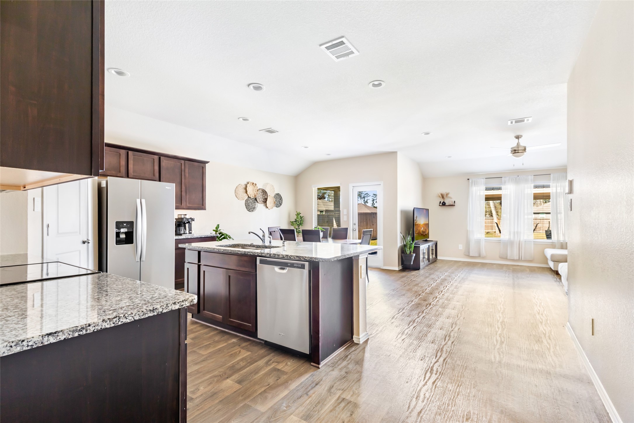 811 Republic Road New Caney, TX 77357 - Photo 22 of 37 This photo showcases a bright, open-concept living area with a modern kitchen featuring granite countertops and dark wood cabinets. The space flows into a cozy living room with large windows, offering ample natural light.