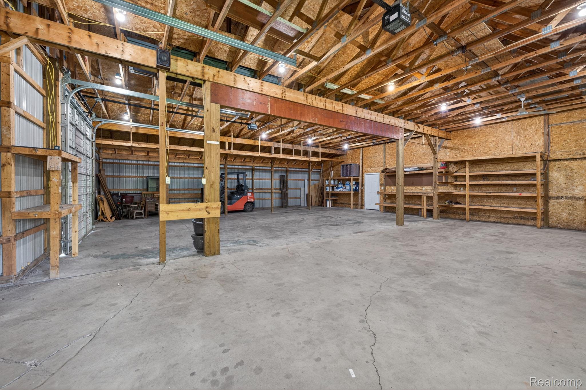9353 Hill Road Swartz Creek, MI 48473 - Photo 76 of 98 Spacious interior warehouse featuring a concrete floor, exposed wood beam ceiling, multiple overhead lighting fixtures, and integrated wood shelving