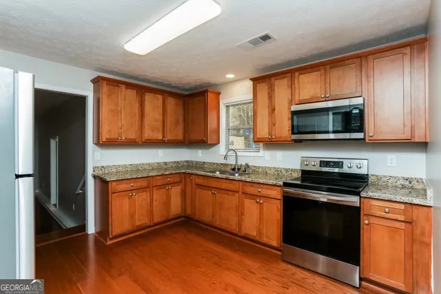 a kitchen with stainless steel appliances granite countertop wooden cabinets a stove top oven a sink and dishwasher with wooden floor