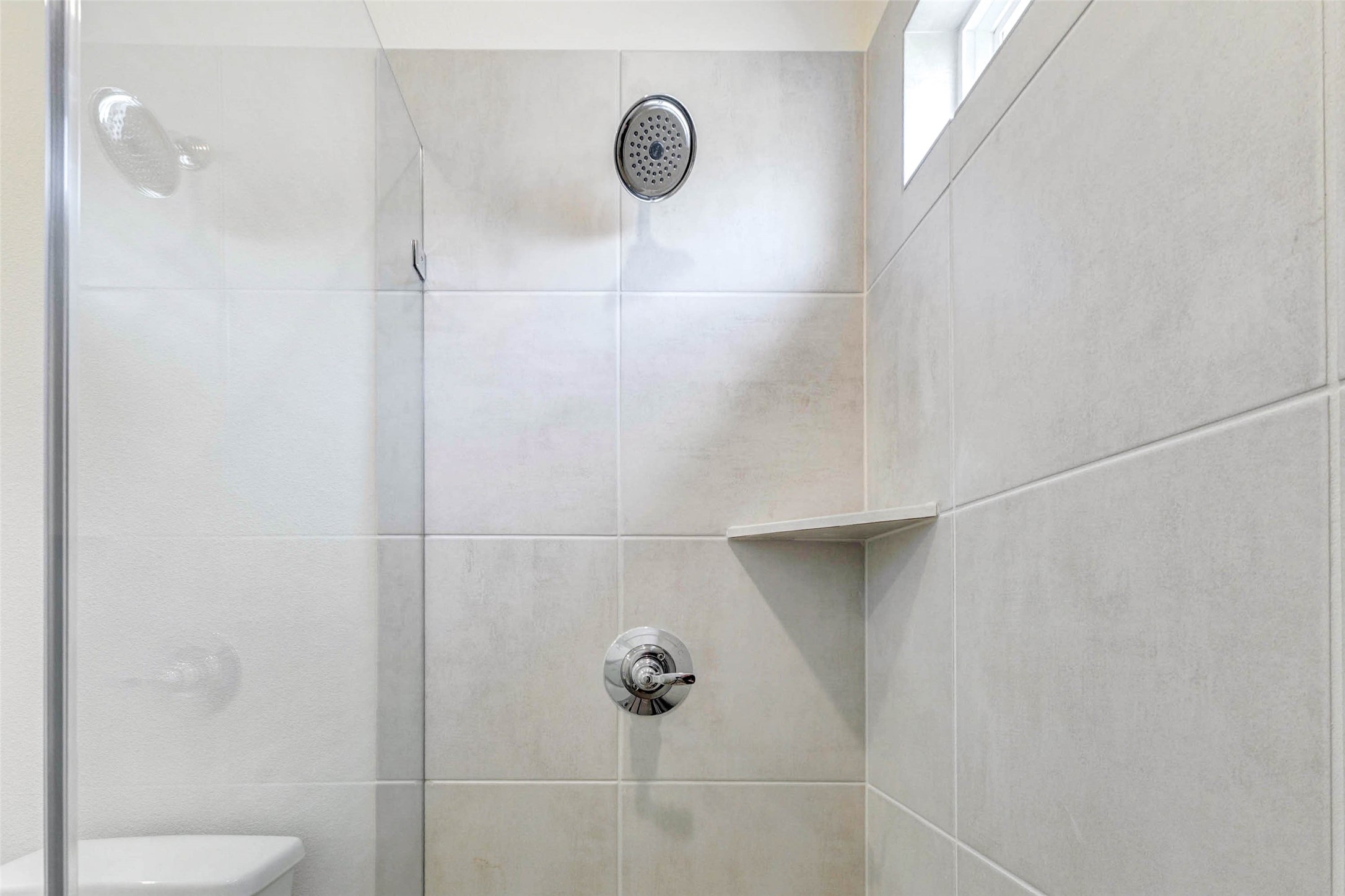 6475 Escondido Drive Rosharon, TX 77583 - Photo 20 of 32 A closer look at the walk-in shower showcases neutral tile surround, chrome shower fixtures, a built-in corner shelf, and a high window that brings in natural light while maintaining privacy. The clean design and simple finishes create a fresh, functional bathroom detail.