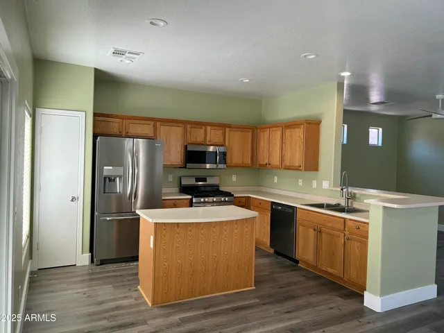 a kitchen with stainless steel appliances granite countertop a refrigerator a sink dishwasher a stove top oven a refrigerator and island with wooden floor