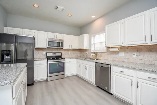 a kitchen with granite countertop white cabinets and stainless steel appliances