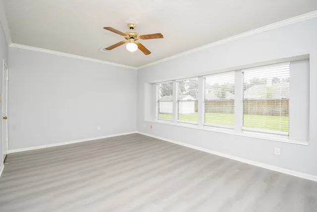 an empty room with wooden floor fan and windows