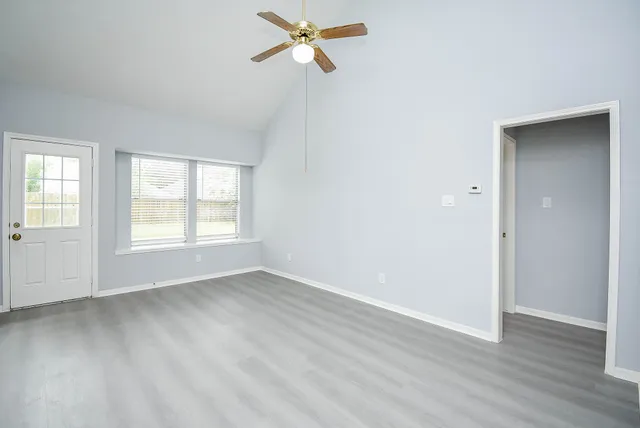 an empty room with wooden floor ceiling fan and windows