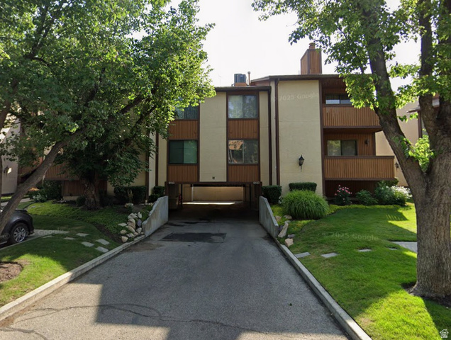 6852 Countrywoods Circle, Unit 5D Midvale, UT 84047 - Photo 38 of 50 Multi-story building featuring tan stucco and wood-finish siding, mature trees, landscaped grounds, and integrated covered parking