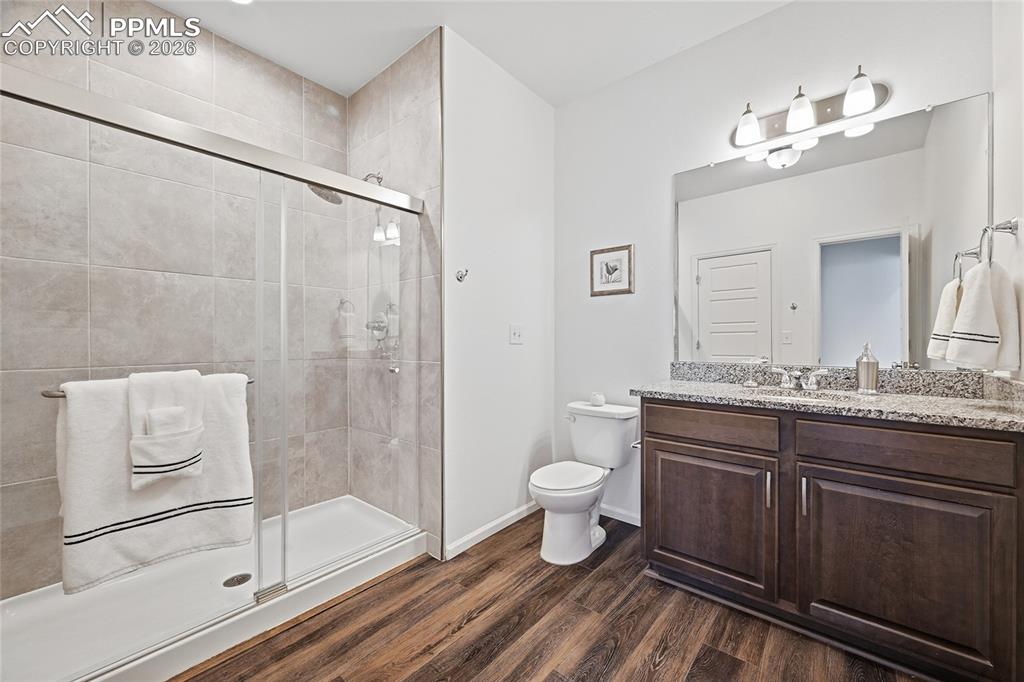 9414 Timberlake Loop Colorado Springs, CO 80927 - Photo 20 of 40 Upper level bathroom, dark wood finish cabinetry, light stone countertops, a stall shower, and dark luxury vinyl wood-style floors