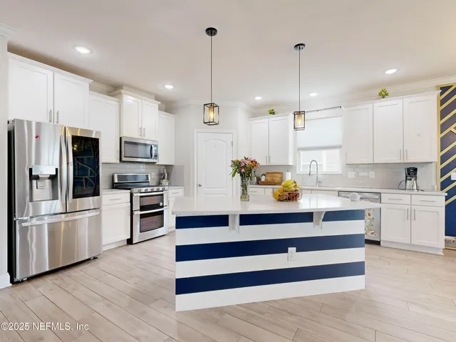 a kitchen with stainless steel appliances kitchen island granite countertop a refrigerator a stove and white cabinets with wooden floors