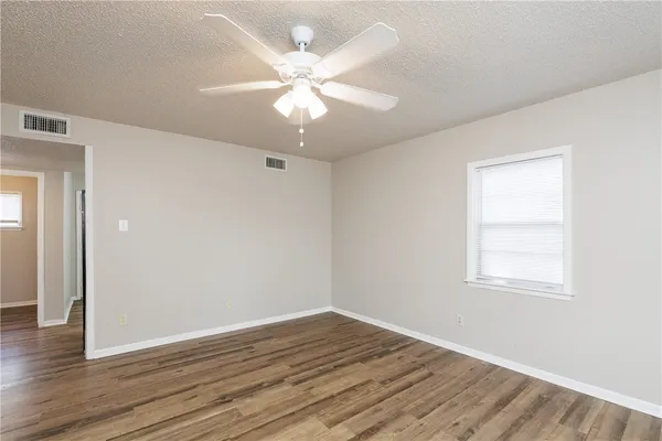 an empty room with wooden floor fan and windows