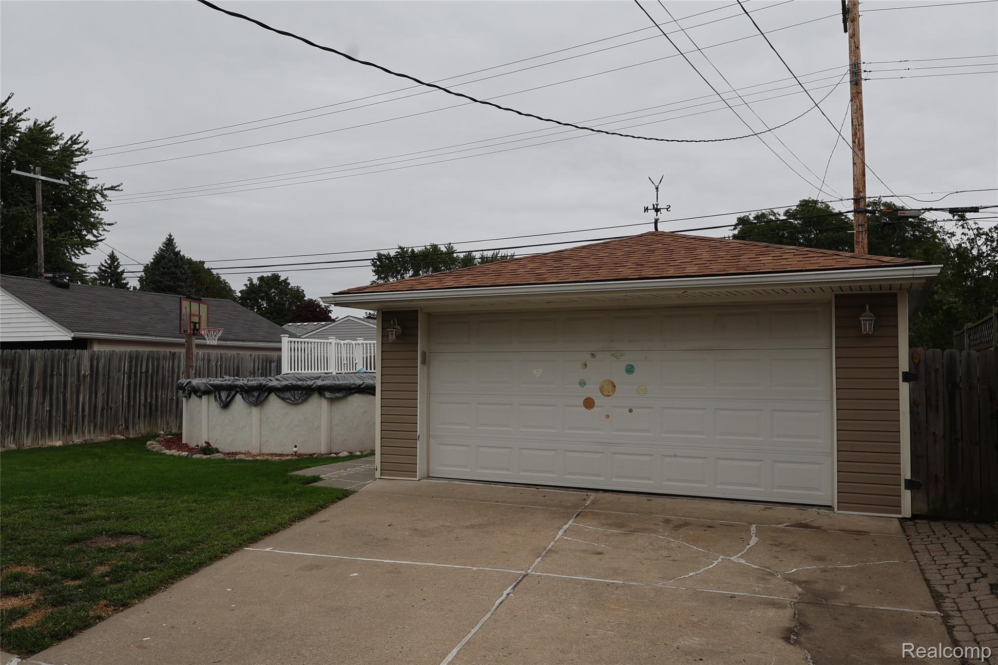 26140 Hayes Road Roseville, MI 48066 - Photo 21 of 21 Detached garage with a shingled roof, exterior lighting, and a white garage door