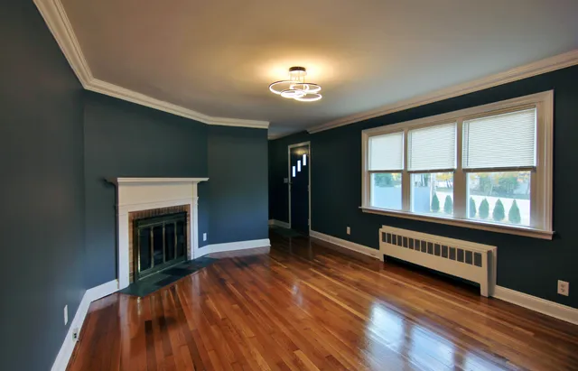 a view of an empty room with wooden floor fireplace and a window