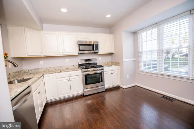 a kitchen with stainless steel appliances white cabinets a sink a stove a microwave and wooden floors