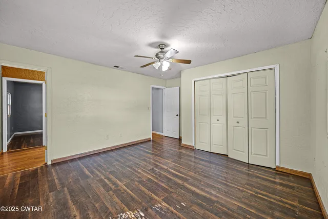 a view of an empty room with wooden floor and a ceiling fan