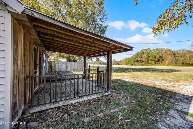 a view of a backyard with lawn chairs under an umbrella with large trees