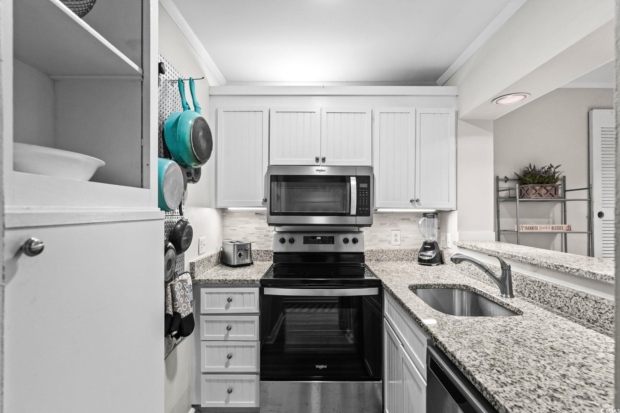415 Ocean Creek Drive, Unit 2346 Myrtle Beach, SC 29572 - Photo 14 of 40 Kitchen featuring stainless steel appliances, light stone counters, tasteful backsplash, white cabinetry, and ornamental molding
