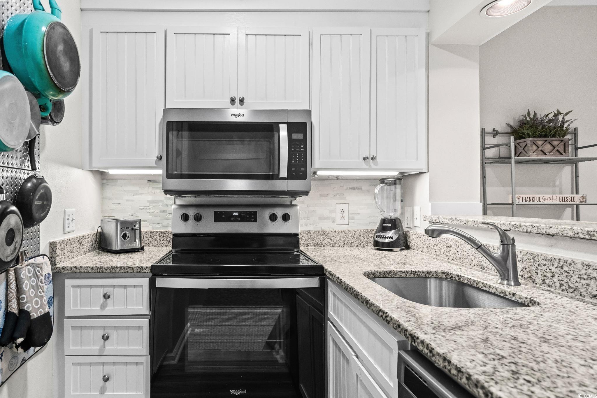 415 Ocean Creek Drive, Unit 2346 Myrtle Beach, SC 29572 - Photo 15 of 40 Kitchen featuring appliances with stainless steel finishes, light stone counters, white cabinetry, and decorative backsplash