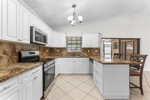 a kitchen with granite countertop a stove a sink dishwasher a refrigerator with a dining table and chairs