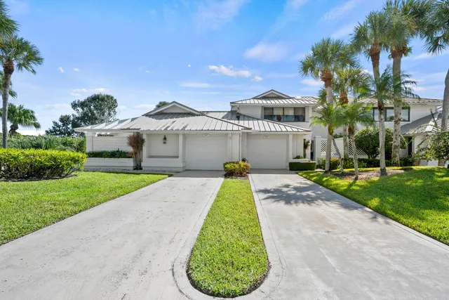 a view of a white house with a small yard and palm trees