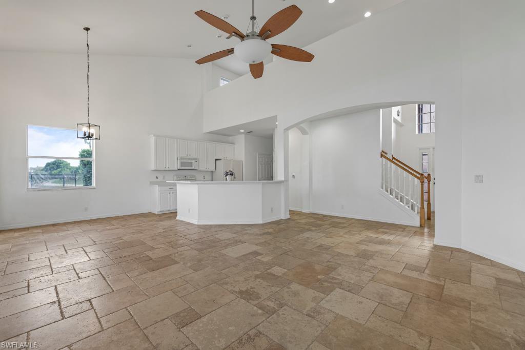 Undisclosed Address Naples, FL 34120 - Photo 7 of 24 Unfurnished living room with high vaulted ceiling, stone tile floors, stairway, a ceiling fan, and a chandelier