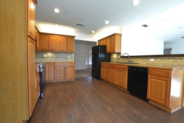 a kitchen with stainless steel appliances granite countertop a refrigerator a stove top oven a sink dishwasher and wooden cabinets with wooden floor