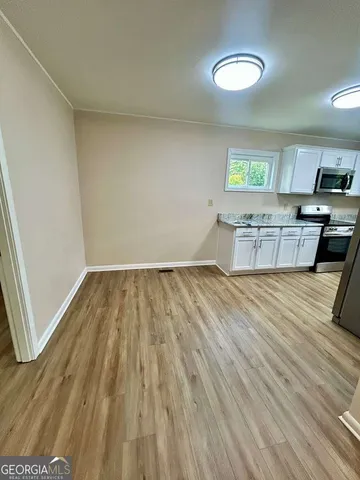 a view of kitchen and empty room with wooden floor