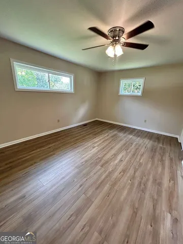 an empty room with wooden floor chandelier fan and windows