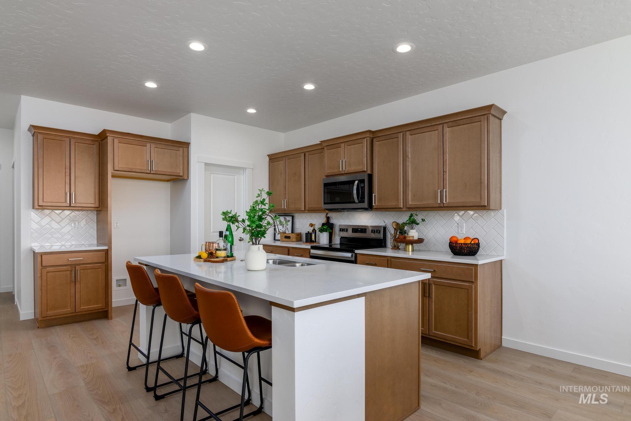 14742 Wing Spread Drive Caldwell, ID 83607 - Photo 5 of 10 Kitchen with a kitchen bar, brown cabinetry, stainless steel appliances, a center island with sink, and light wood-type flooring