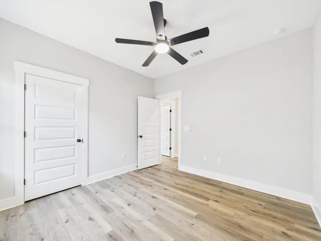 an empty room with wooden floor fan and windows