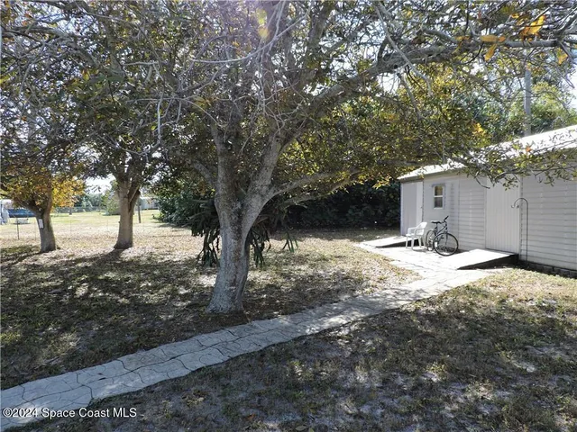 a backyard of a house with table and chairs under a large tree