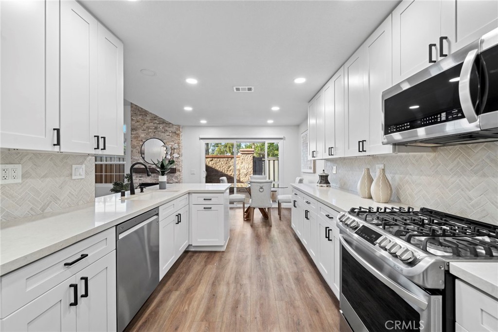 13615 Almond Street Tustin, CA 92782 - Photo 11 of 54 a kitchen with stainless steel appliances a sink dishwasher stove and white cabinets with wooden floor
