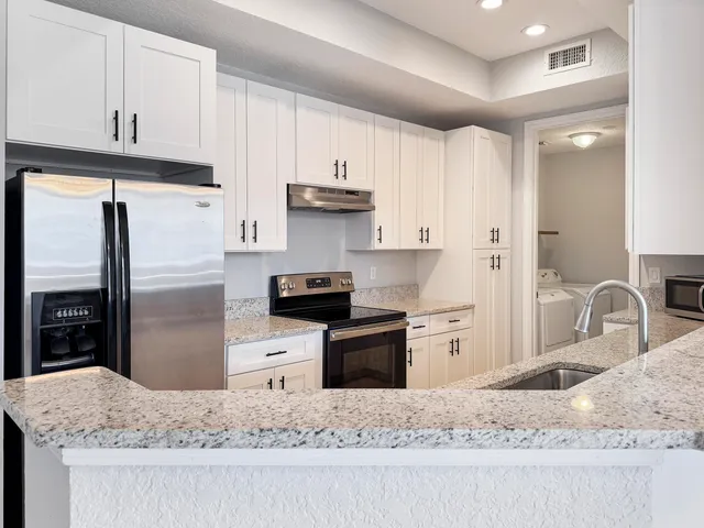 a kitchen with stainless steel appliances granite countertop a refrigerator a stove and a sink