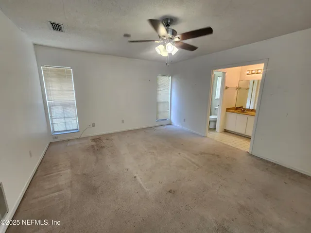 an empty room with chandelier fan and windows