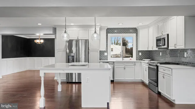a large white kitchen with stainless steel appliances granite countertop a stove and a wooden floors